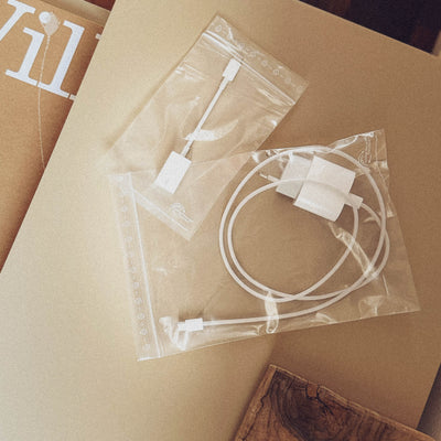Two transparent plastic bags with various small white electronic parts and cables, lying on a brown cardboard surface.