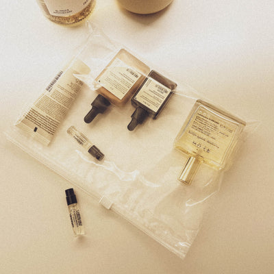Un sac en plastique transparent ouvert rempli de divers petits échantillons de cosmétiques, dont des flacons avec des pipettes, des tubes et un vaporisateur, couchés sur une surface claire et légèrement brillante.